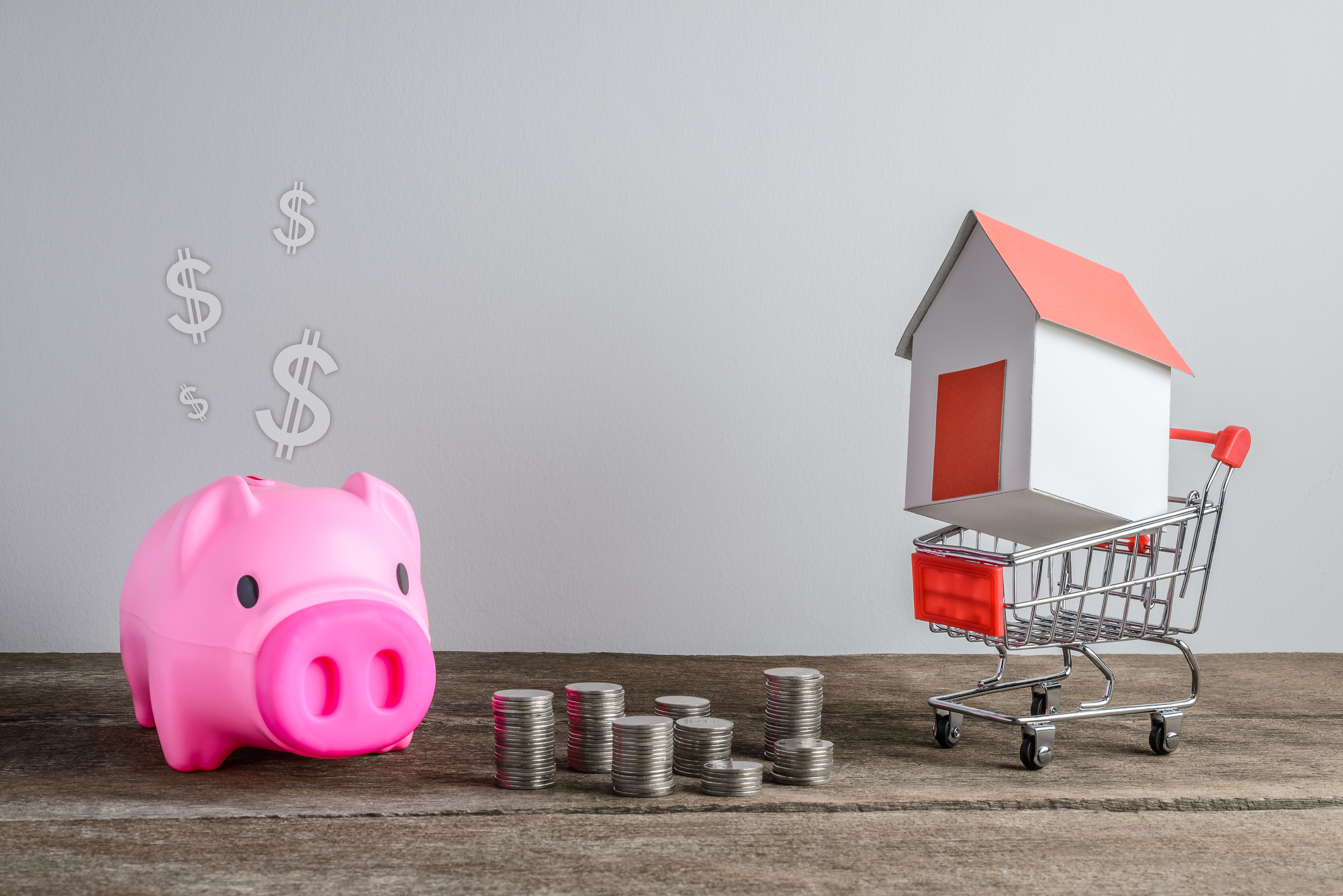House model in shopping cart and row of coin money and piggy bank on wooden desk. Real Estate market, Trading Estate, Mortgage Concepts